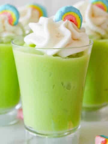 Close up of shot glass with green pudding topped with whipped cream and marshmallow.