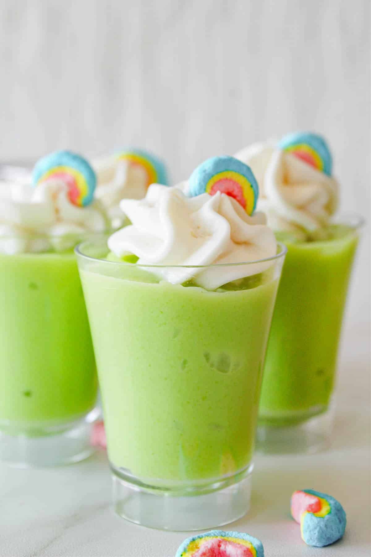 Green pudding in a shot glass topped with whipped cream and marshmallows.