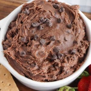 white bowl with chocolate brownie batter dip with chocolate chips mixed in and strawberries and graham crackers on the side.