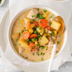closeup of a white bowl of creamy chicken pot pie soup with diced carrots, potatoes and peas.