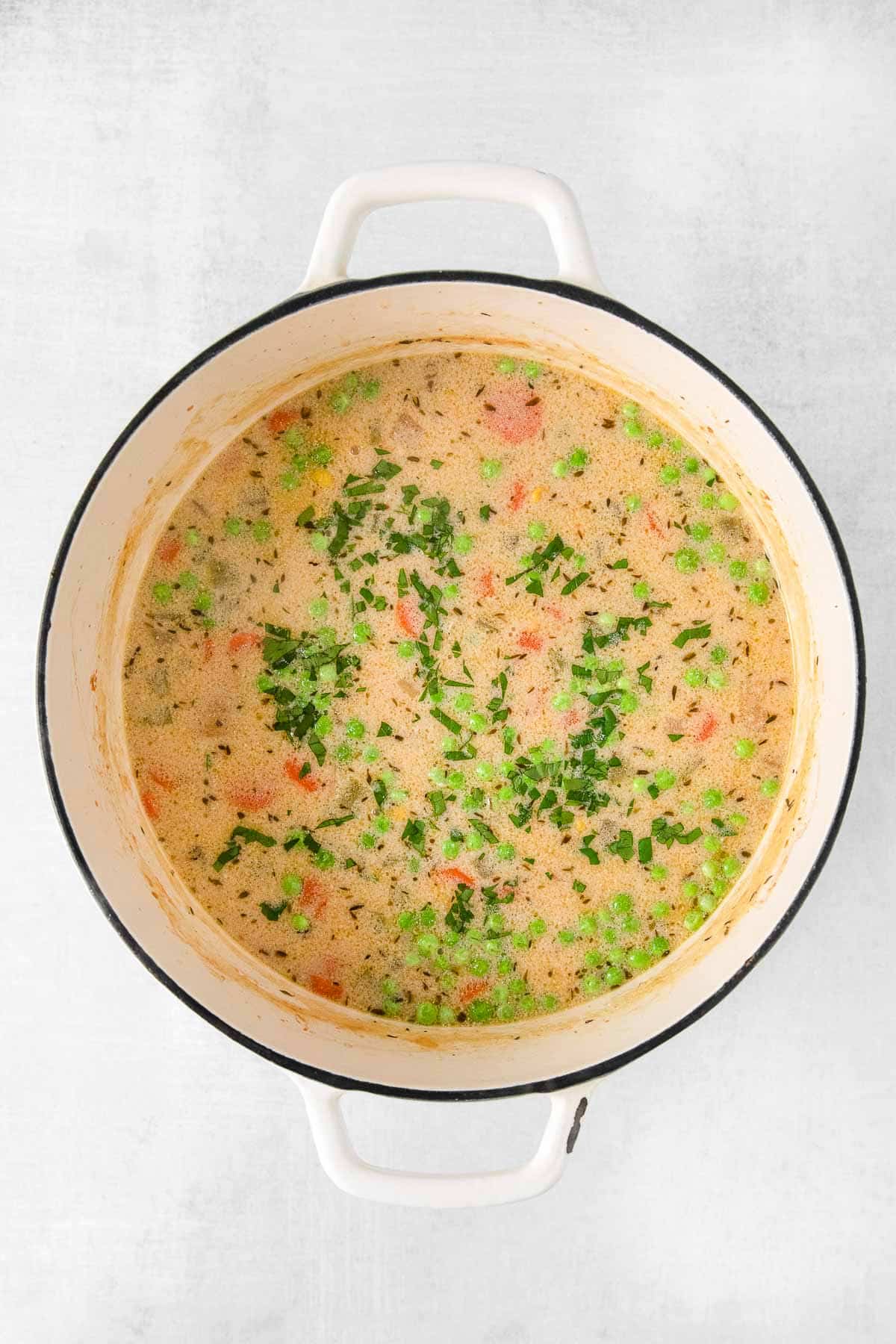 creamy soup with peas and carrots in a white dutch oven soup pot.