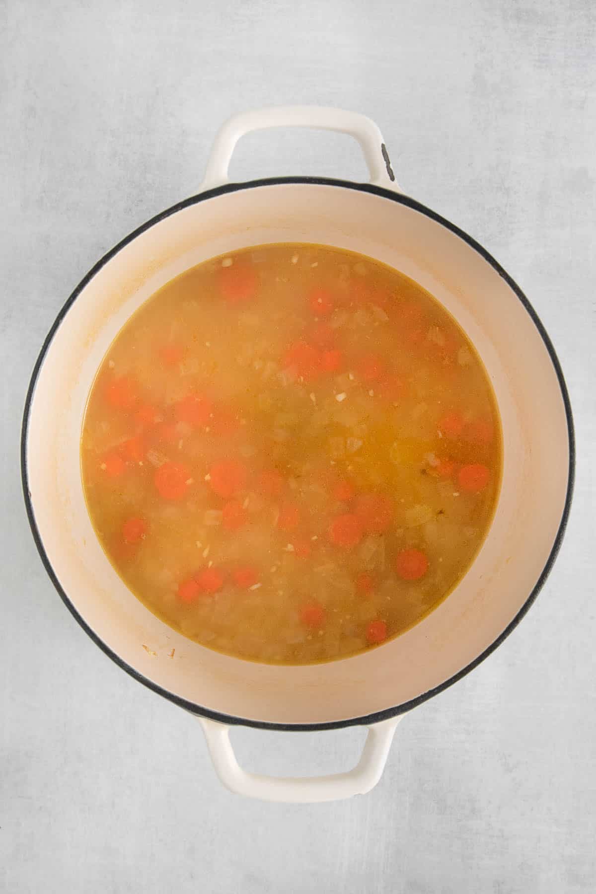 white soup pot with chicken broth and cooked carrots and onions.