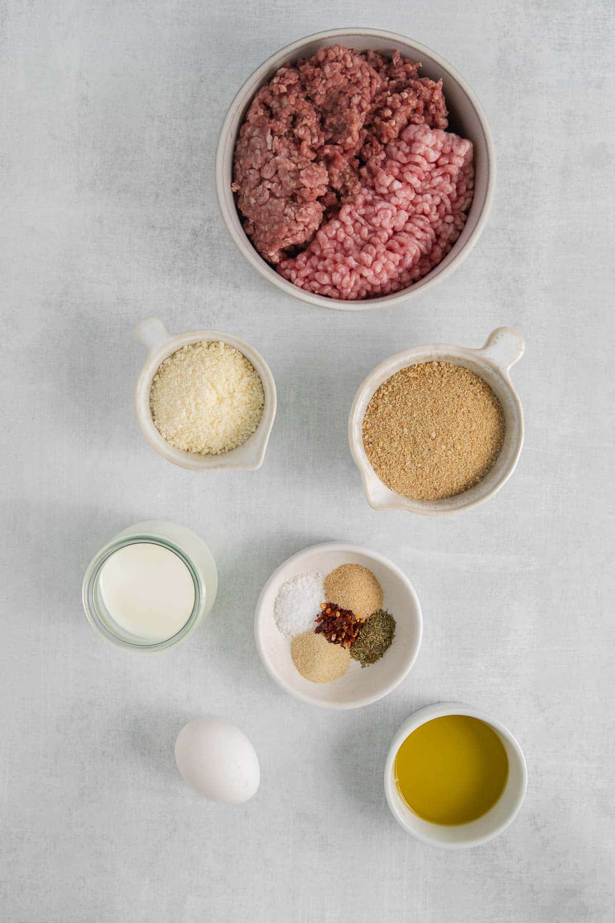 ingredients for homemade meatballs - raw meat, egg, breadcrumbs, parmesan cheese, spices and oil.
