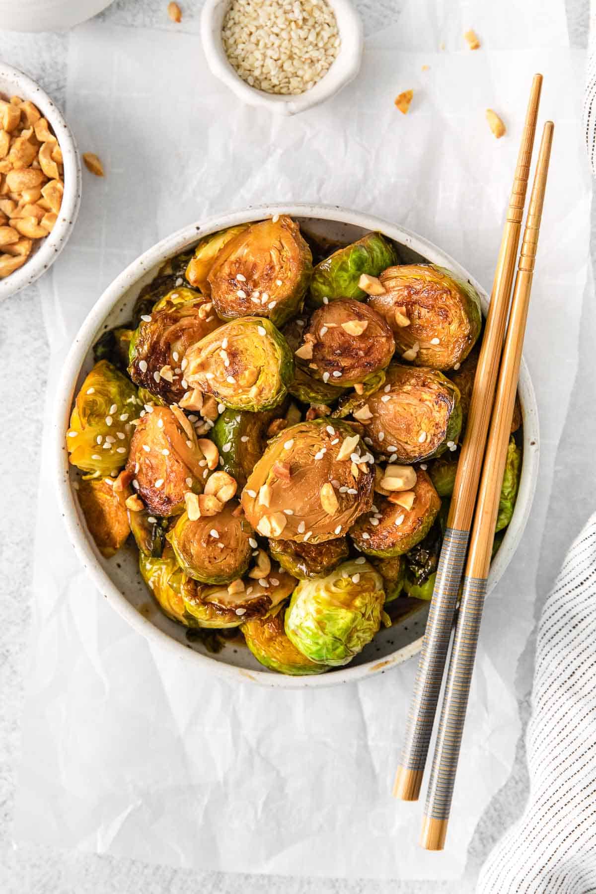 white bowl with kung pao brussel sprouts topped with chopped peanuts and sesame seeds.