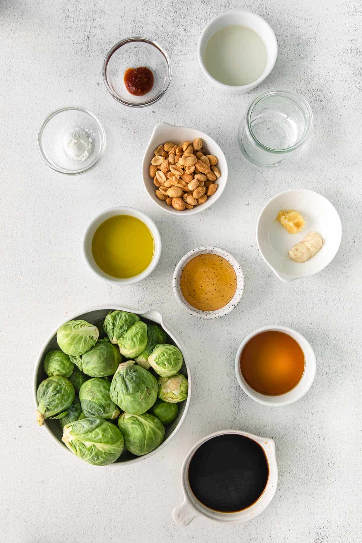 several small bowls with ingredients for Kung Pao Brussel Sprouts - brussel sprouts, olive oil, sesame oil, soy sauce, honey, garlic, ginger, peanuts.