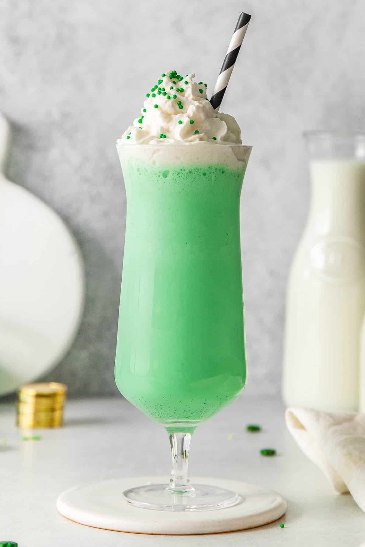 tall glass of green milkshake topped with whipped cream and green sprinkles.