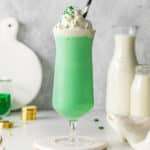 tall glass of green milkshake topped with whipped cream and green sprinkles.