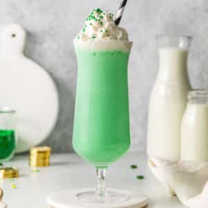 tall glass of green milkshake topped with whipped cream and green sprinkles.