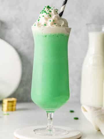 tall glass of green milkshake topped with whipped cream and green sprinkles.