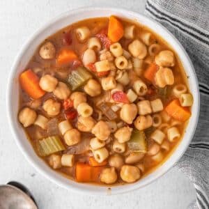 white bowl full of vegetarian minestrone soup with chickpeas in tomato broth.
