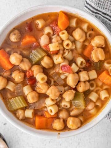 white bowl full of vegetarian minestrone soup with chickpeas in tomato broth.