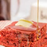 stack of three red velvet pancakes with maple syrup being poured over.