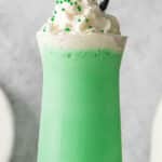 green milkshake topped with whipped and green sprinkles in a tall glass