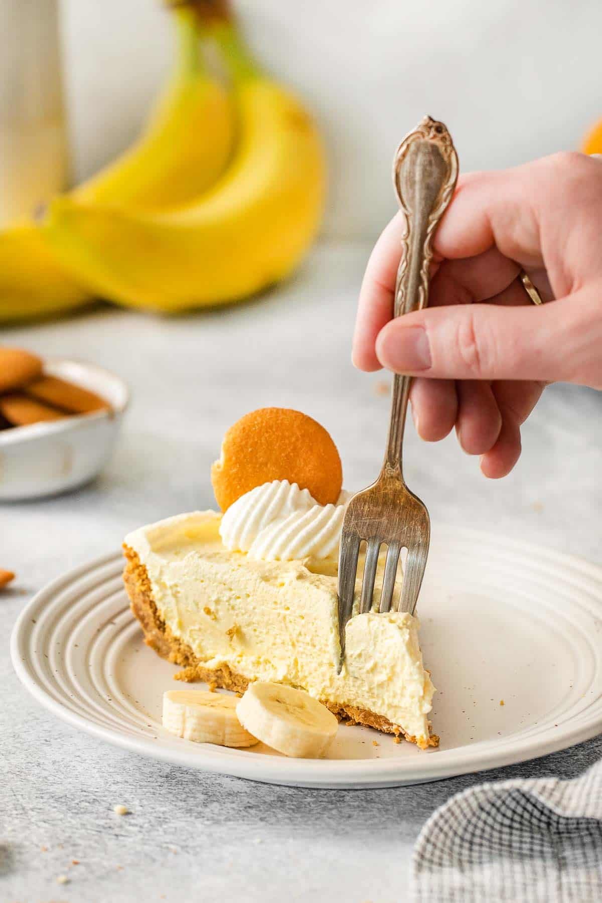 Silver fork inserted into a slice of banana pudding pie on white plate.