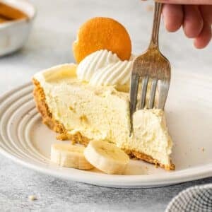 Silver fork inserted into a piece of banana pudding pie on white plate.
