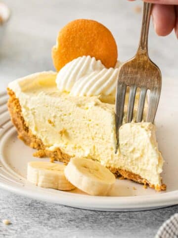 Silver fork inserted into a piece of banana pudding pie on white plate.