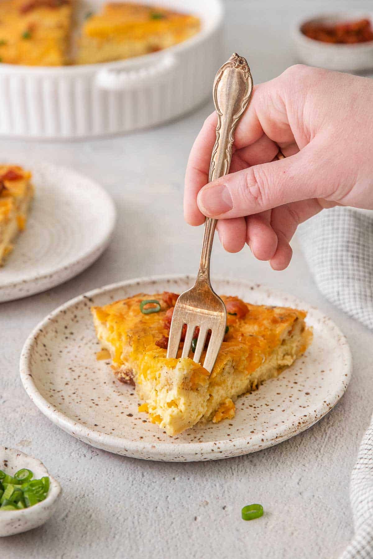 Slice of bisquick quiche on a white plate with a fork taking a bite.