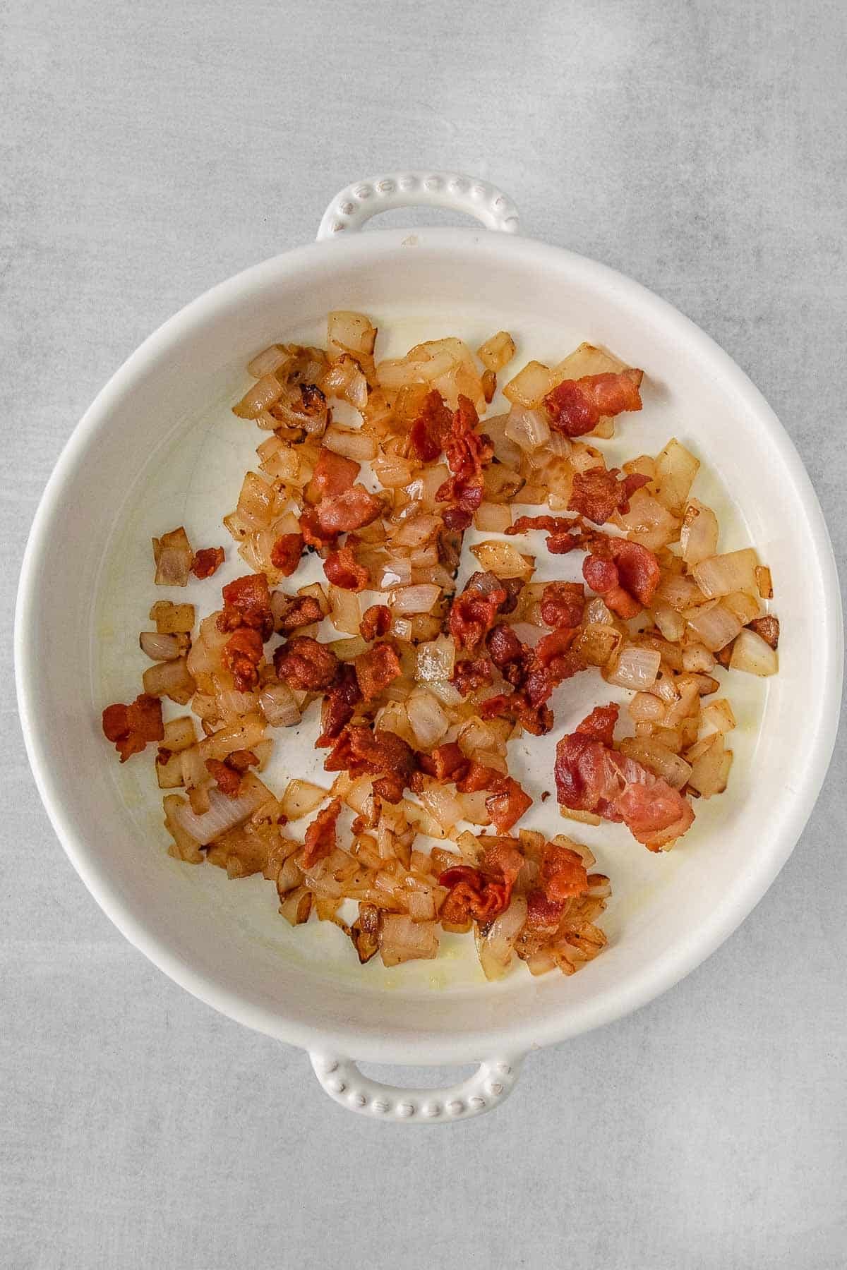 White bowl containing cooked bacon and onion mixed together.