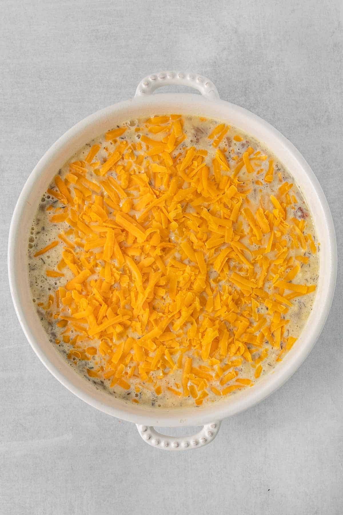 Egg mixture poured over bacon and onion in bowl and topped with cheddar cheese.