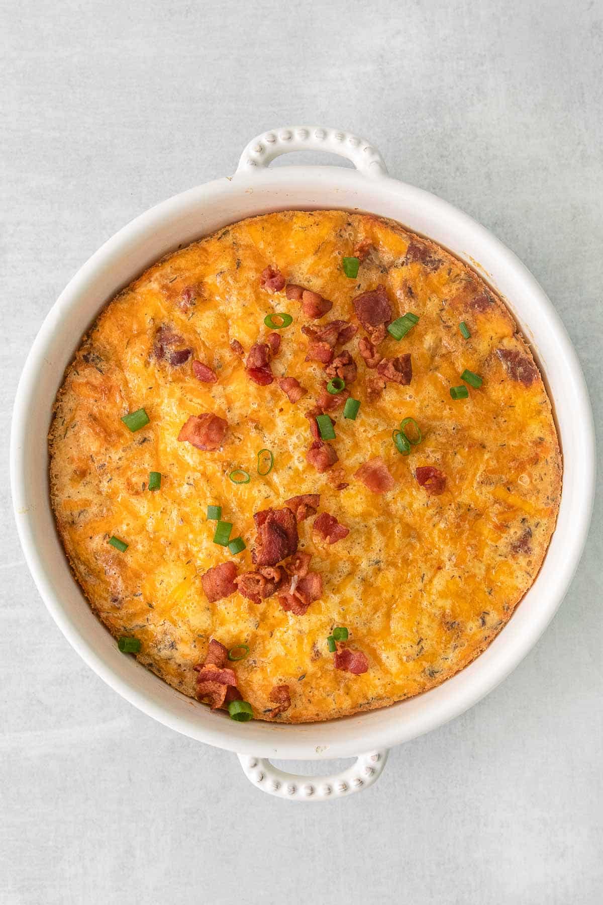 Baked Bisquick quiche in white bowl topped with green onion and bacon bits.