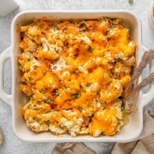 Cheesy cauliflower casserole with two spoons in white casserole dish.