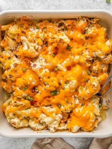 Cheesy cauliflower casserole with two spoons in white casserole dish.