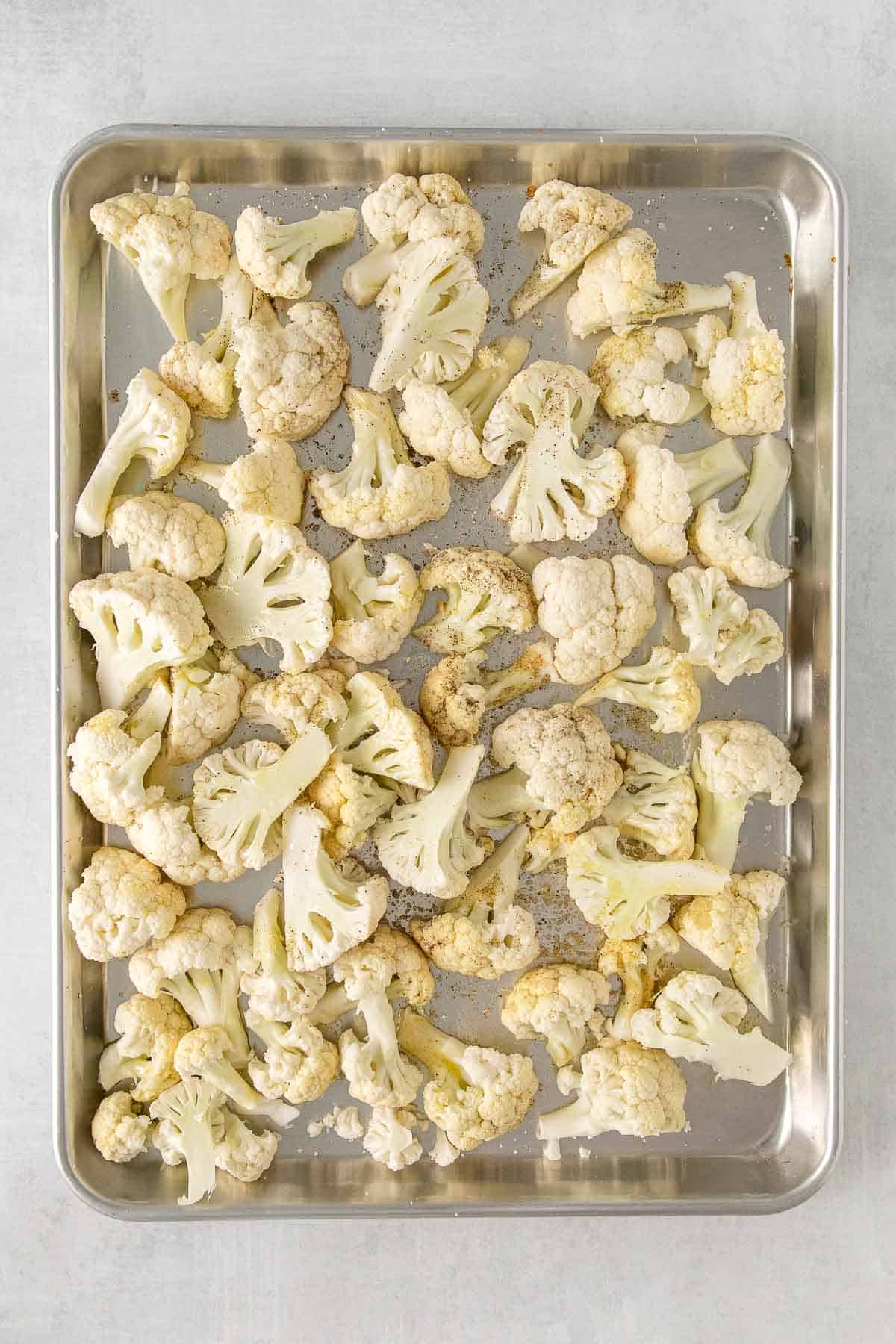 Uncooked cauliflower florets on baking sheet with seasonings sprinkled over.