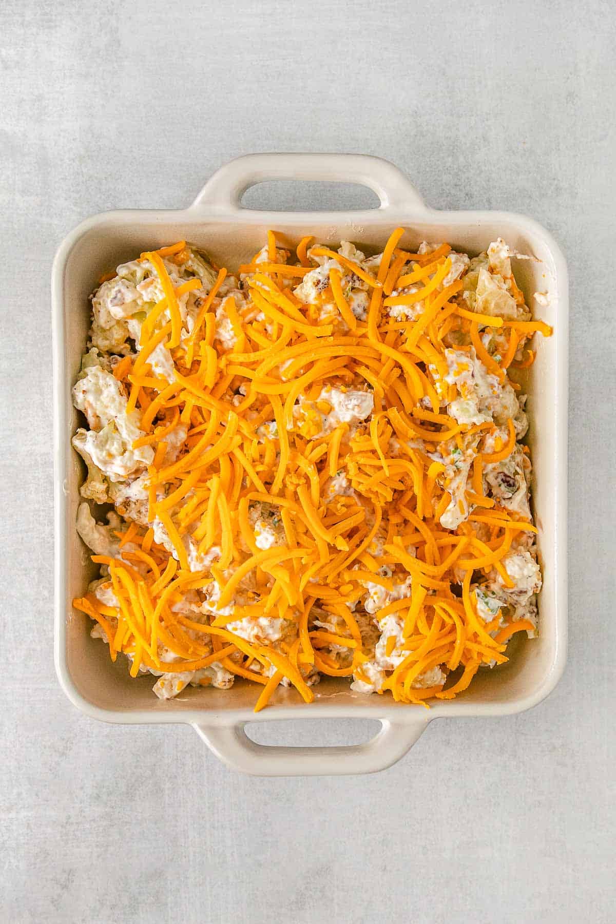 Cauliflower mixture in a baking dish topped with shredded cheddar cheese.