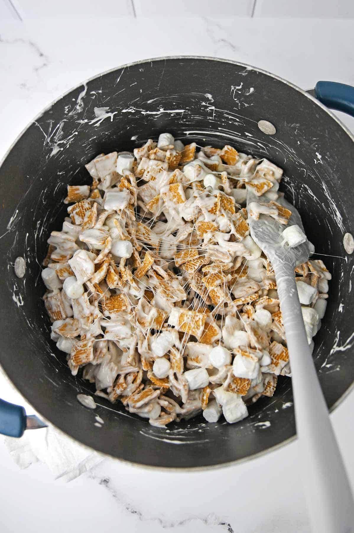 Golden grahams cereal stirred into the melted marshmallow mixture in a large pot.