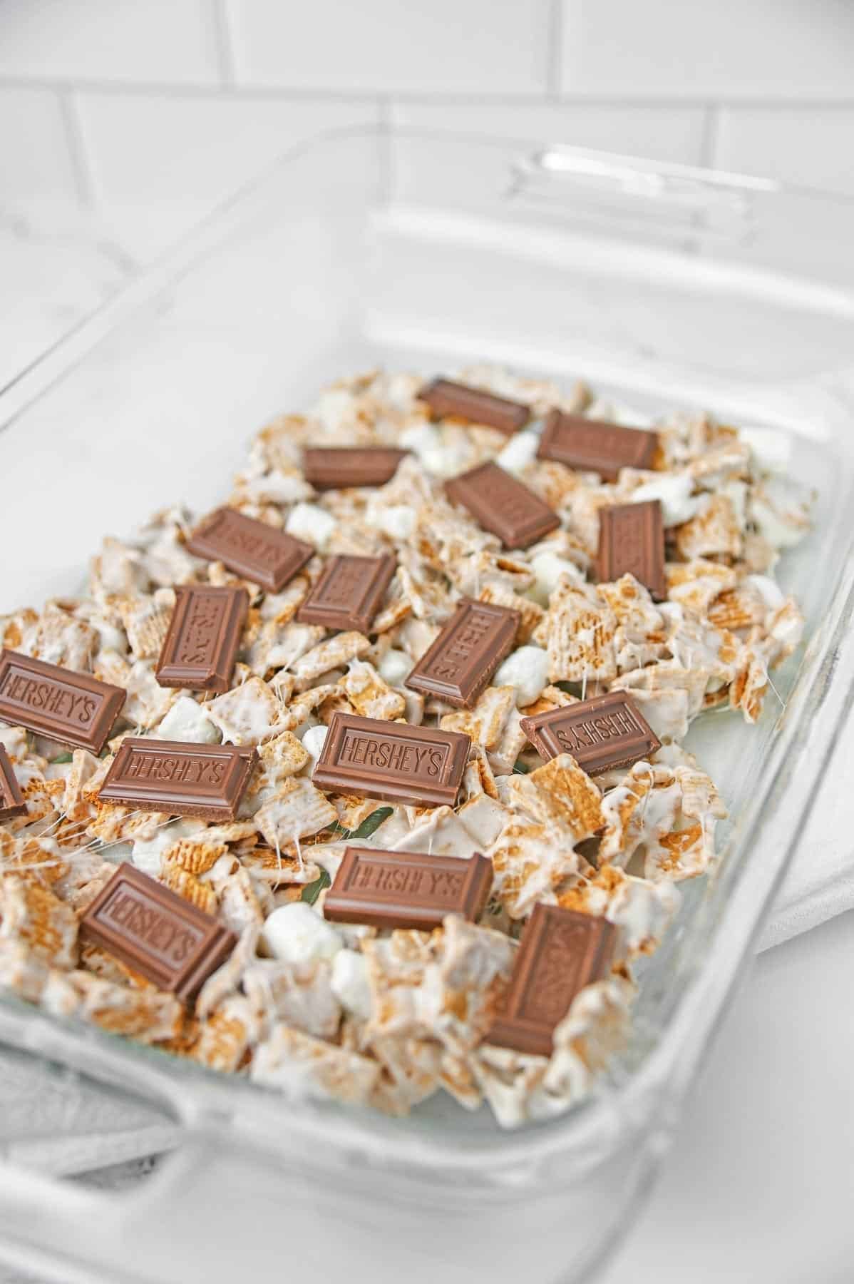 The cereal marshmallow mixture pressed evenly to the bottom of the glass baking dish with chocolate bar pieces laid over.