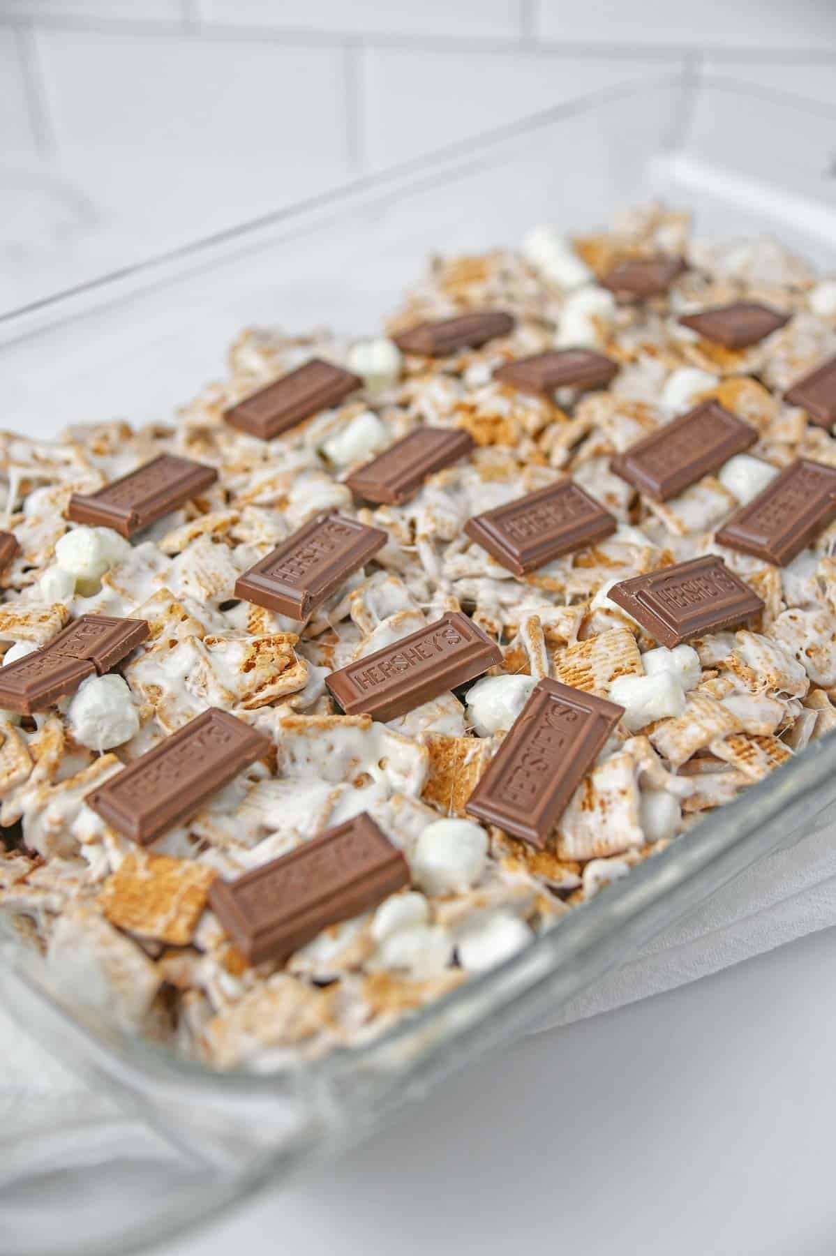 The cereal marshmallow mixture in glass baking dish with chocolate bar pieces on top.