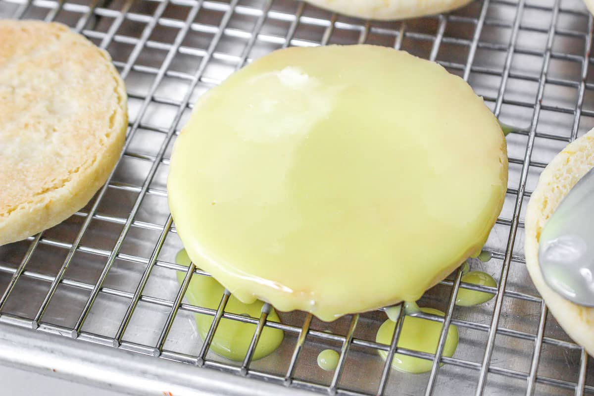 Glazed lemon shortbread cookie on cookie rack with lemon glaze dripping onto baking sheet.