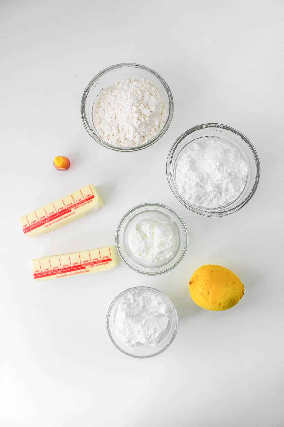 Several small bowls with ingredients for Lemon Shortbread Cookies - powdered sugar, flour, cornstarch, 2 stick of butter and lemon.