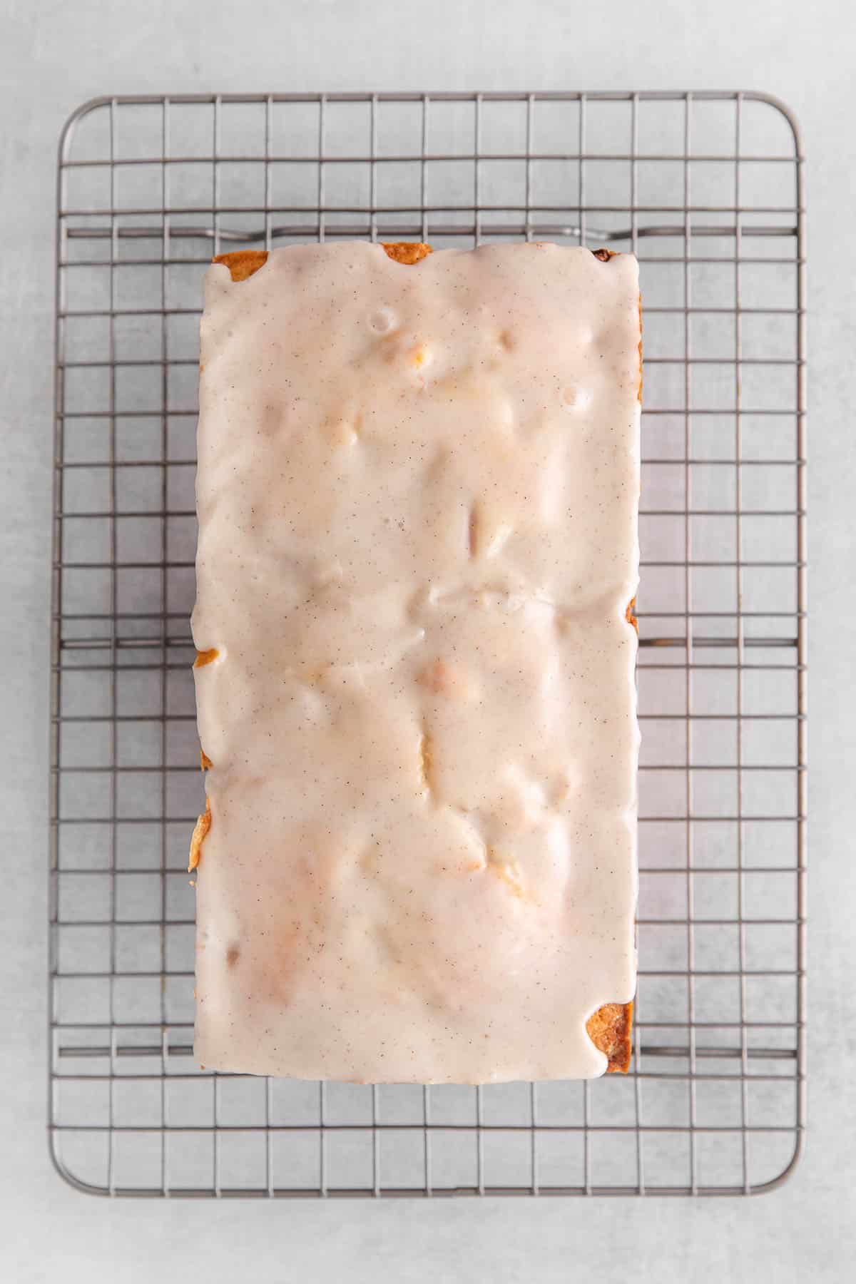 Loaf of peach cobbler pound cake topped with vanilla glaze on a wire cooling rack.