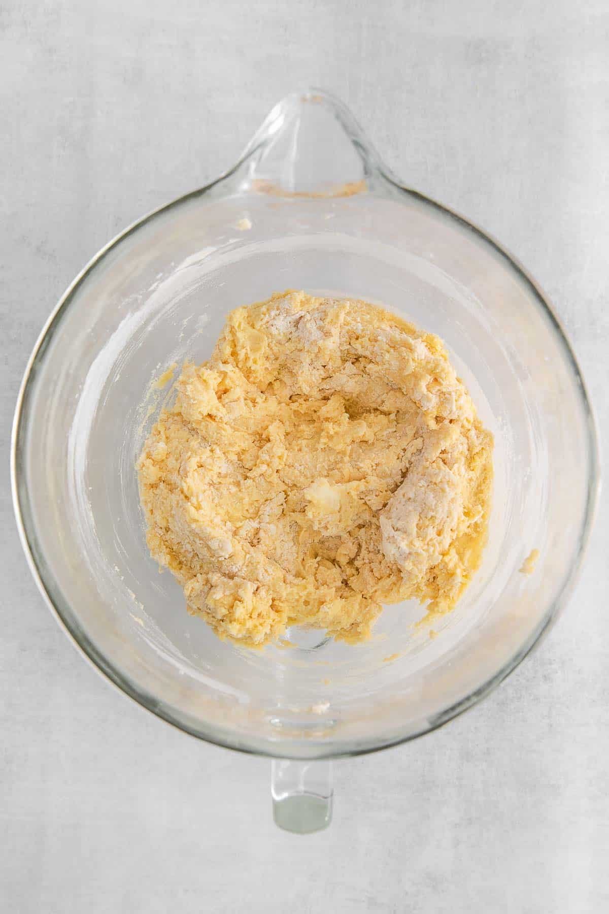 Flour added to mixture of butter, sugar, eggs and vanilla in a glass mixing bowl.