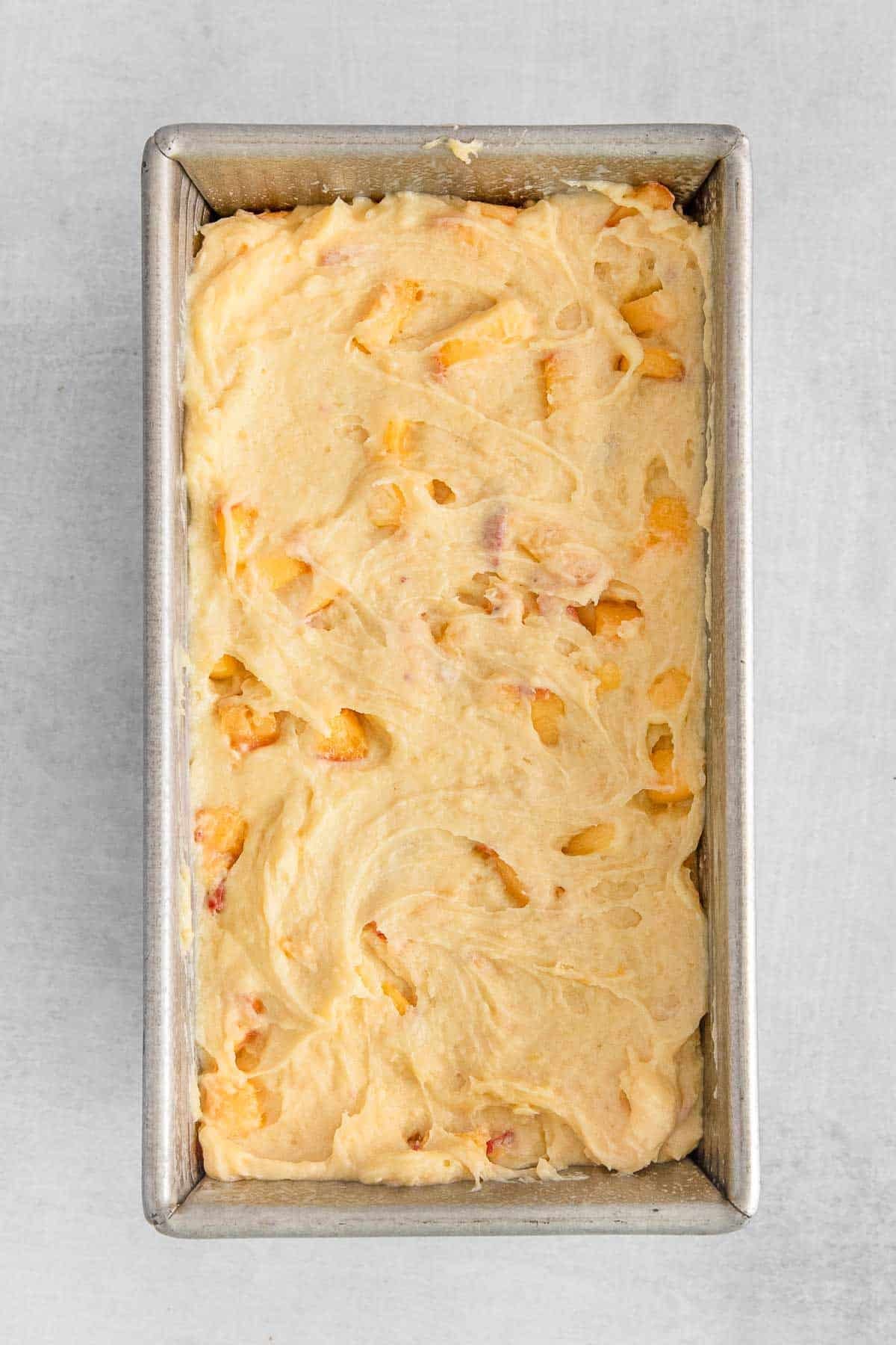 Baking pan containing peach cobbler pound cake batter with peach slices.