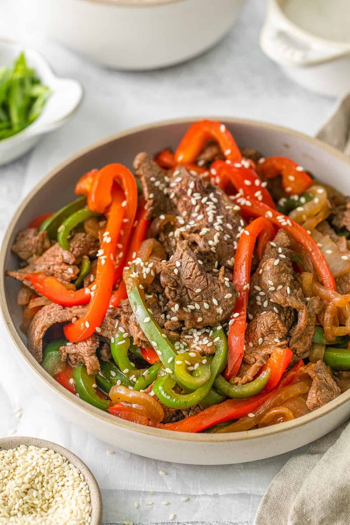 Bowl of pepper steak with green and red bell peppers topped with sesame seeds.