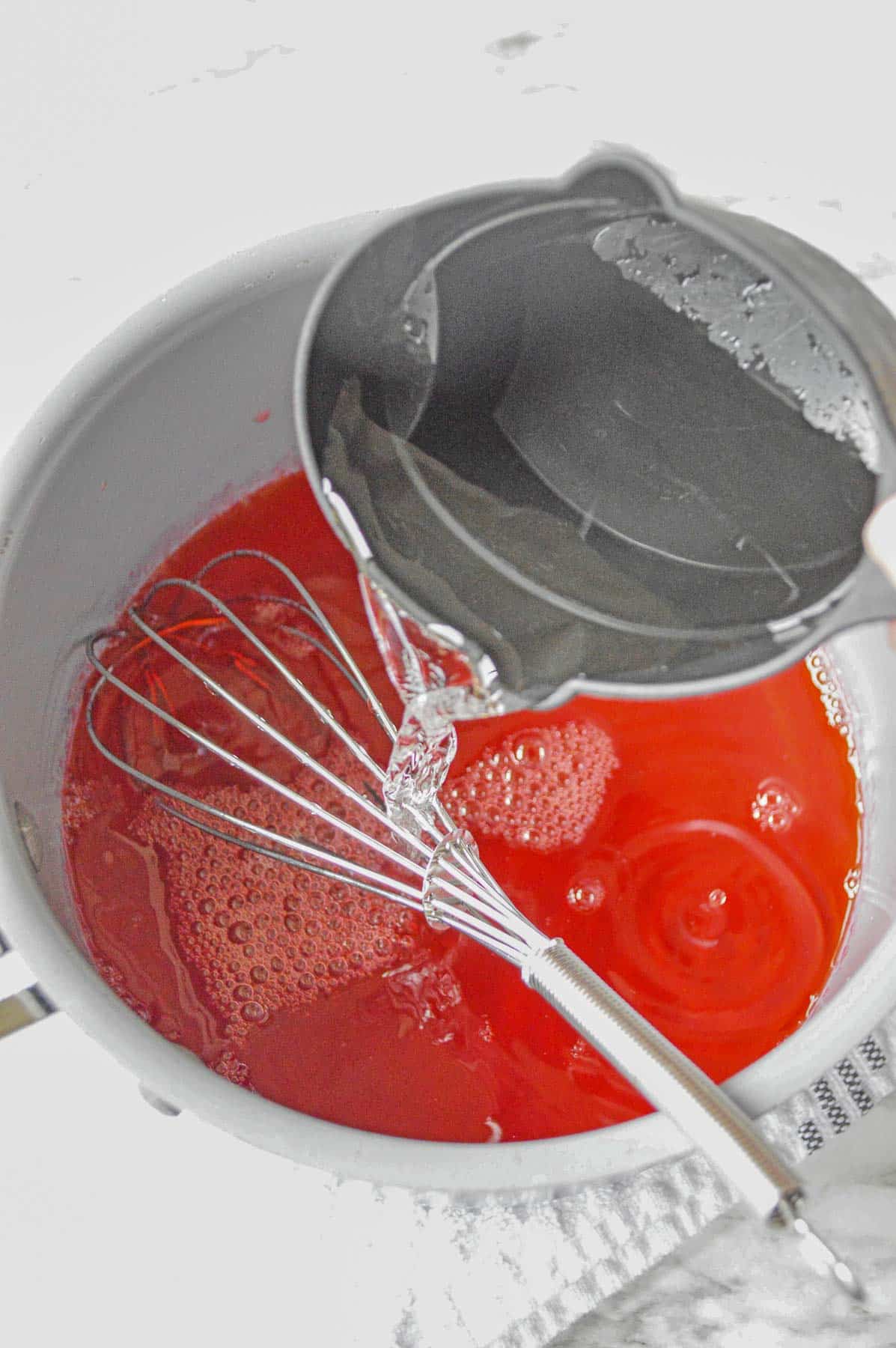 ½ cup of cold water being poured into medium sauce pan of strawberry jello.