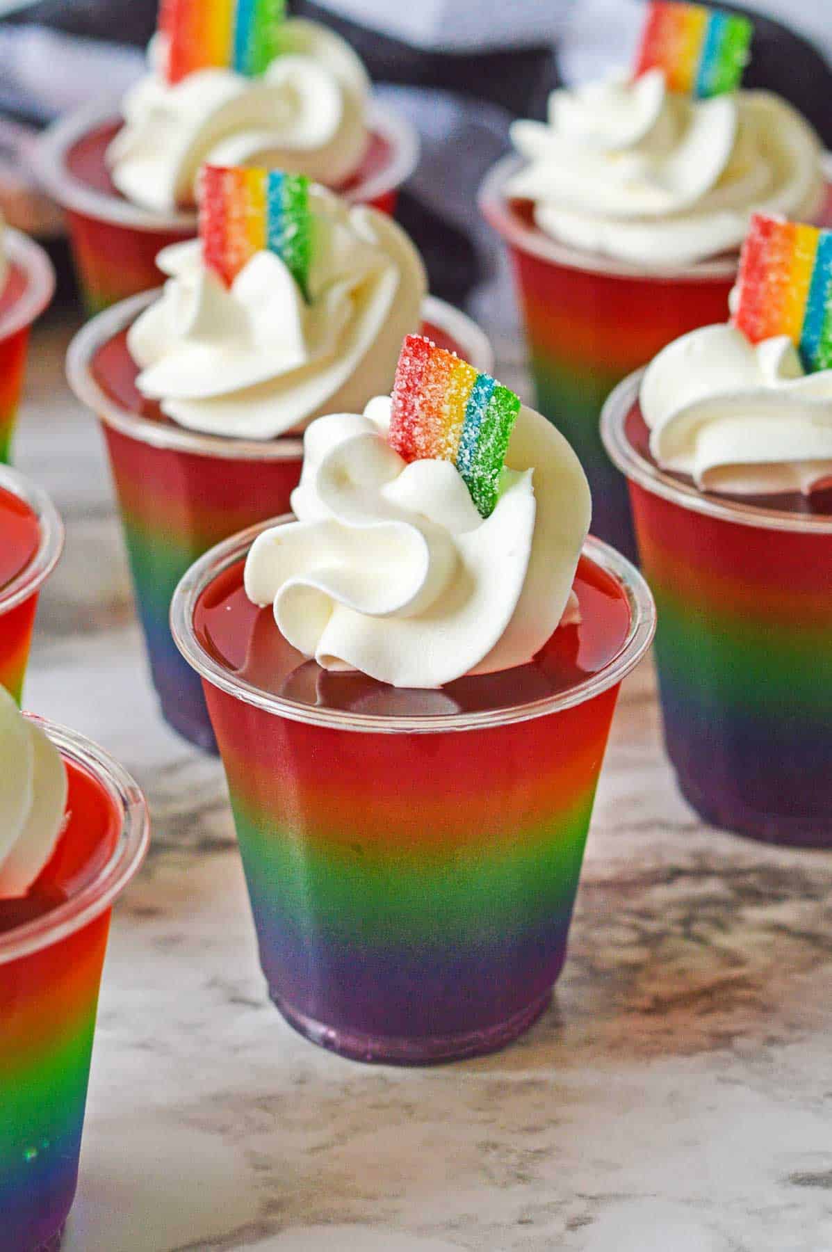 Several rainbow jello shots topped with cool whip and small airhead xtreme pieces.
