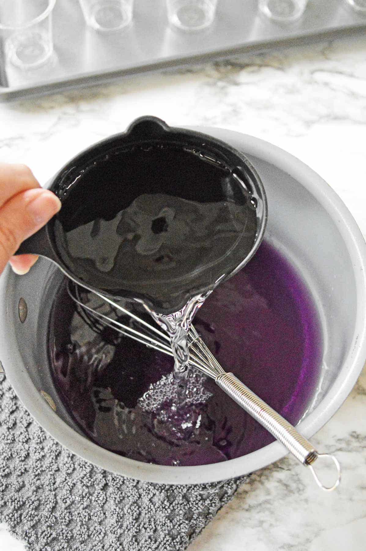 ½ cup of cold water being poured into medium sauce pan of grape jello.