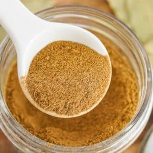 white spoon scooping apple pie spice out of a small glass jar.