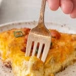 Slice of bisquick quiche on a white plate with a fork taking a bite.