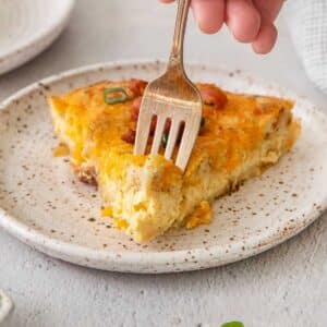 Slice of bisquick quiche on a white plate with a fork taking a bite.