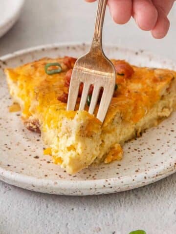 Slice of bisquick quiche on a white plate with a fork taking a bite.