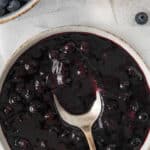 white bowl of homemade blueberry sauce with a spoon in the sauce.