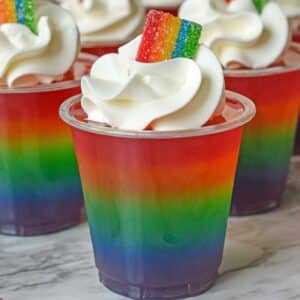 rainbow jello shots topped with whipped cream and rainbow candy.