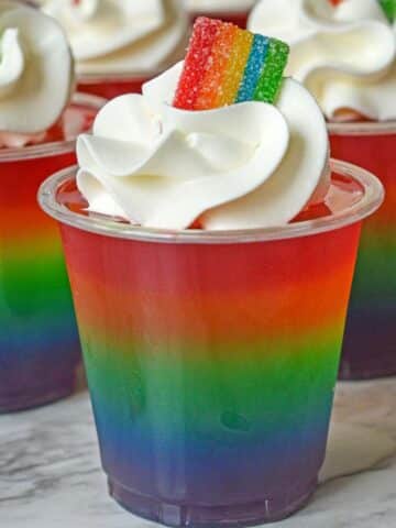 rainbow jello shots topped with whipped cream and rainbow candy.