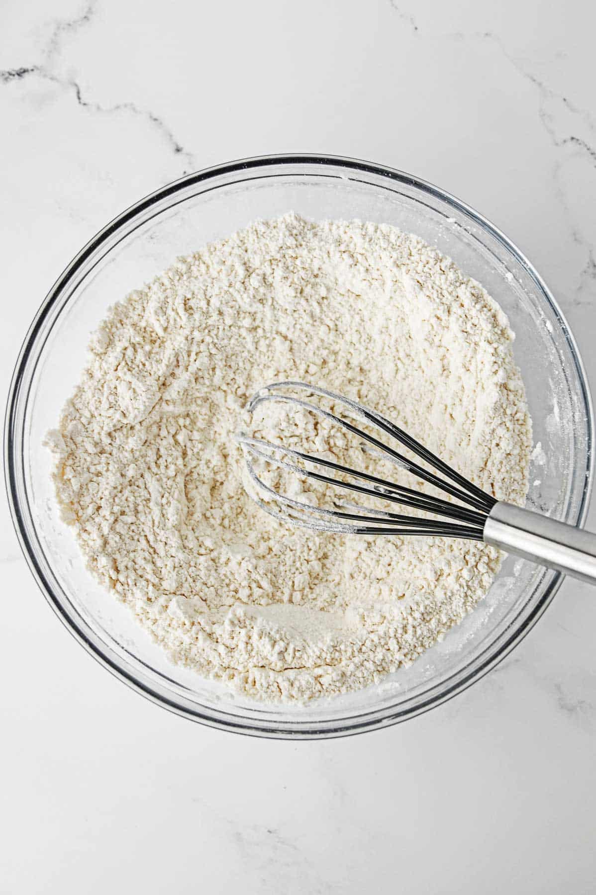 a glass mixing bowl with flour and a whisk.