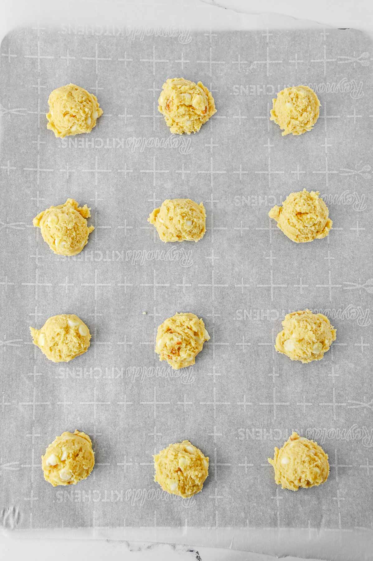 twelve cookie dough balls on parchment lined cookie sheet.