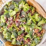 White bowl of broccoli salad with two wooden spoons.